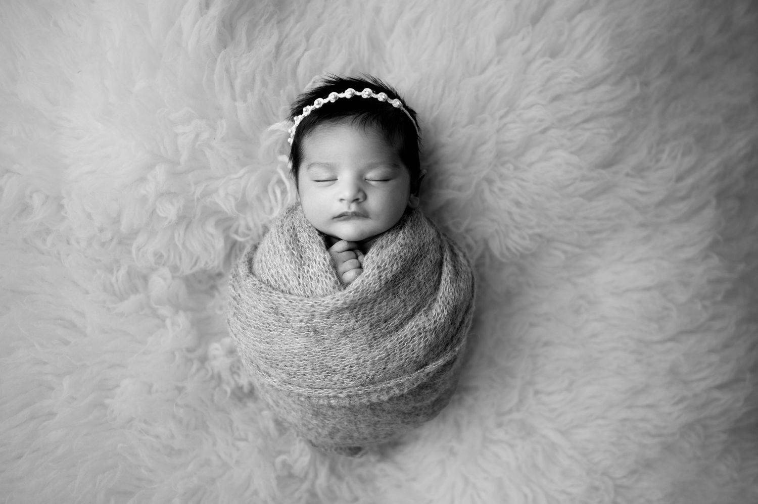 Black and white portrait of swaddled sleeping newborn on fluffy backdrop.