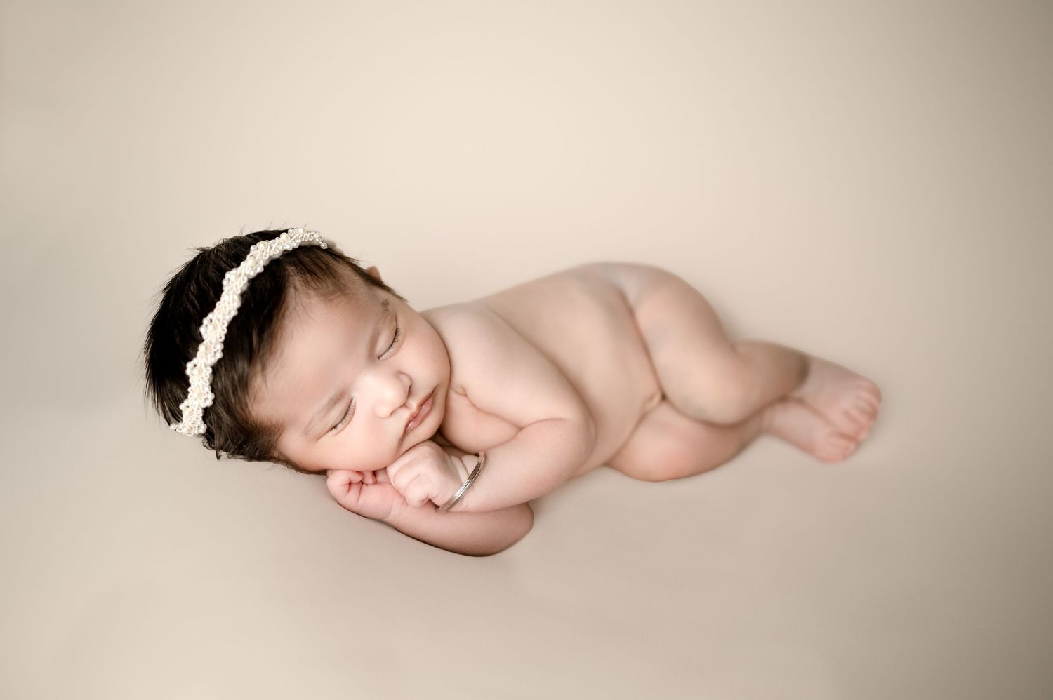 Peaceful newborn sleeping on cream background wearing delicate lace headband.