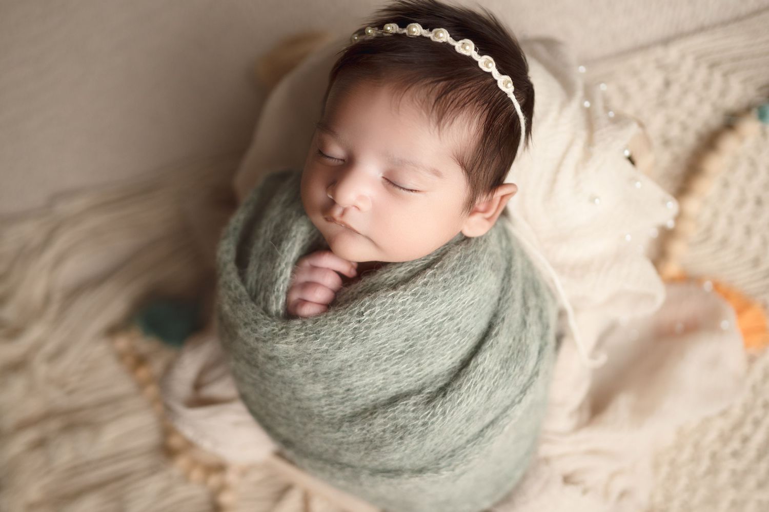 Sleeping newborn wrapped in sage green swaddle on cream textured backdrop.