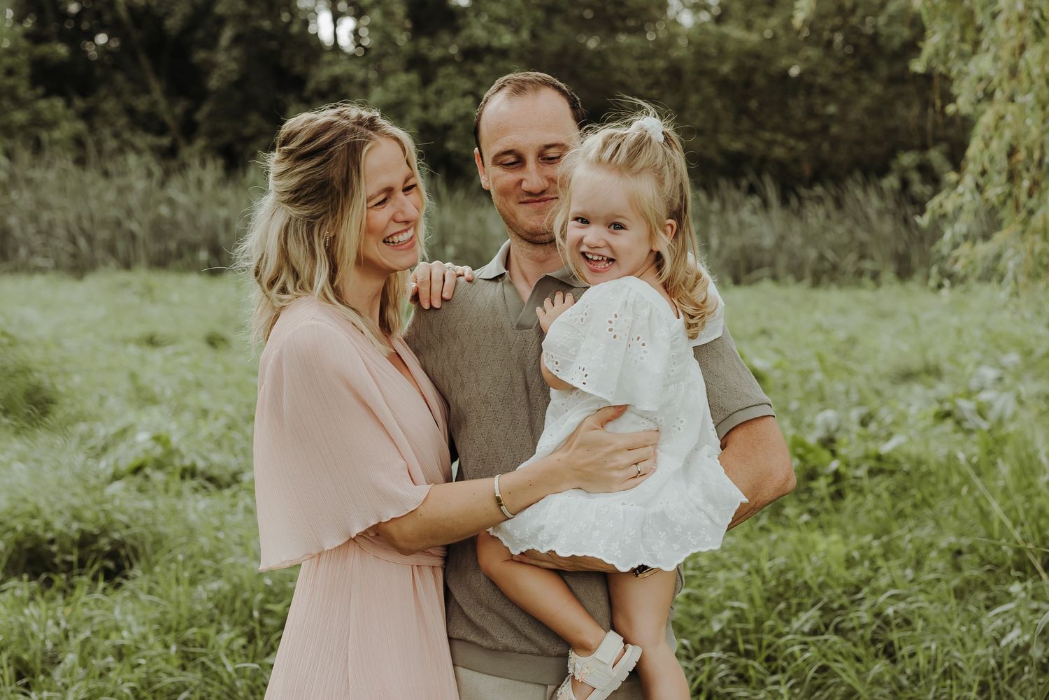 Natural outdoor family portrait with soft lighting and green foliage background.