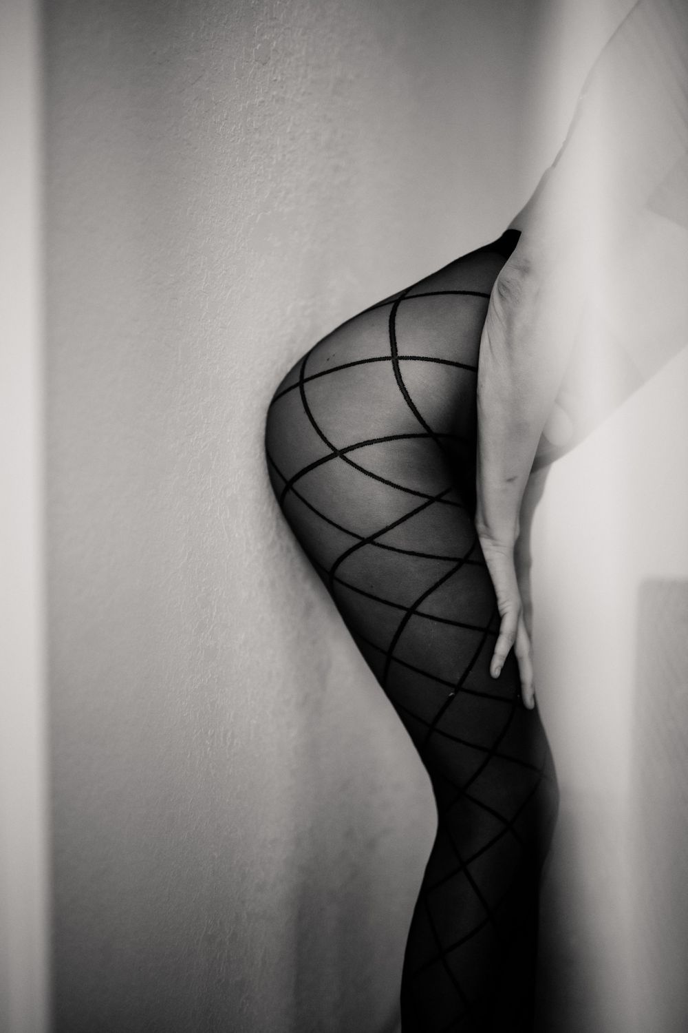Abstract black and white art photograph of patterned stockings against a wall.