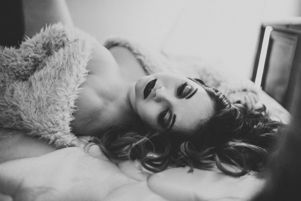 Intimate black and white portrait on soft bedding with moody lighting.