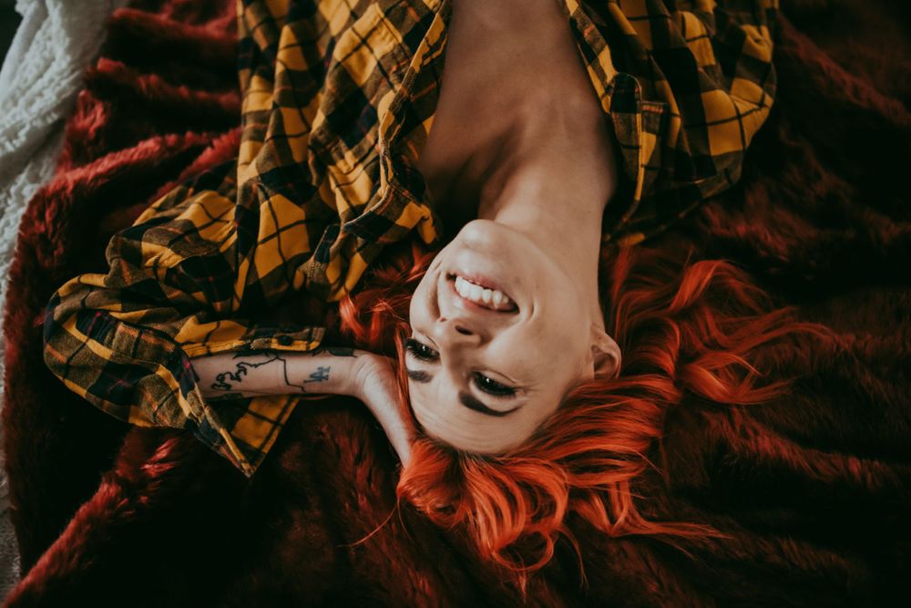 Artistic overhead portrait with vibrant red hair against patterned fabric.