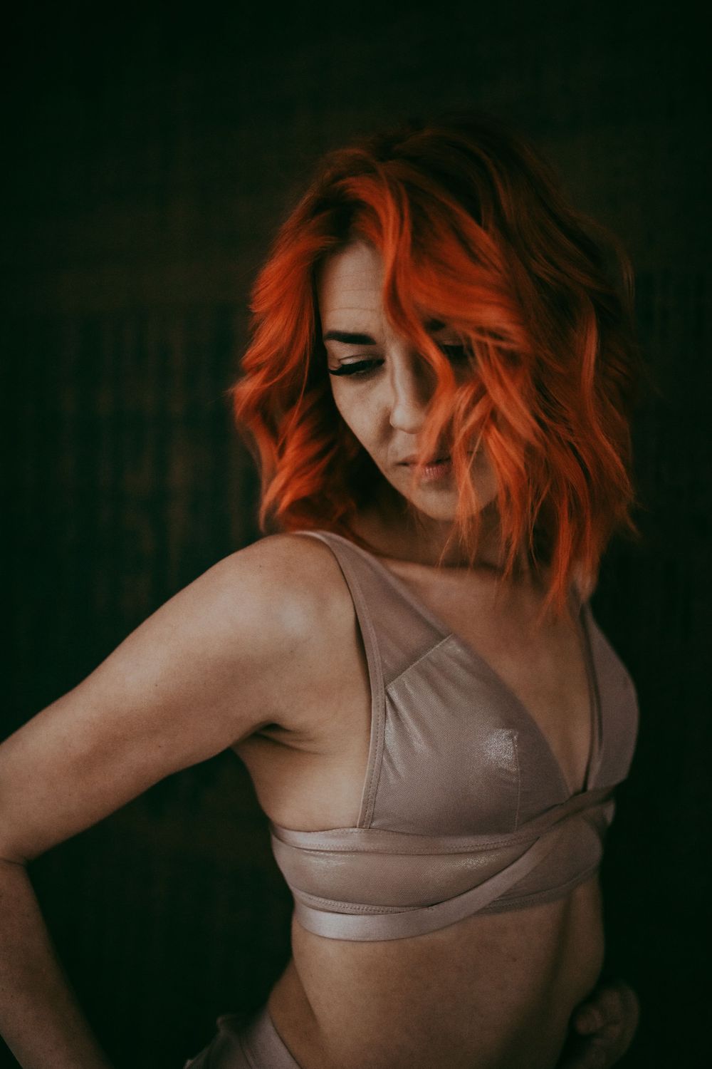 Moody portrait with bright orange hair in neutral toned athletic wear.