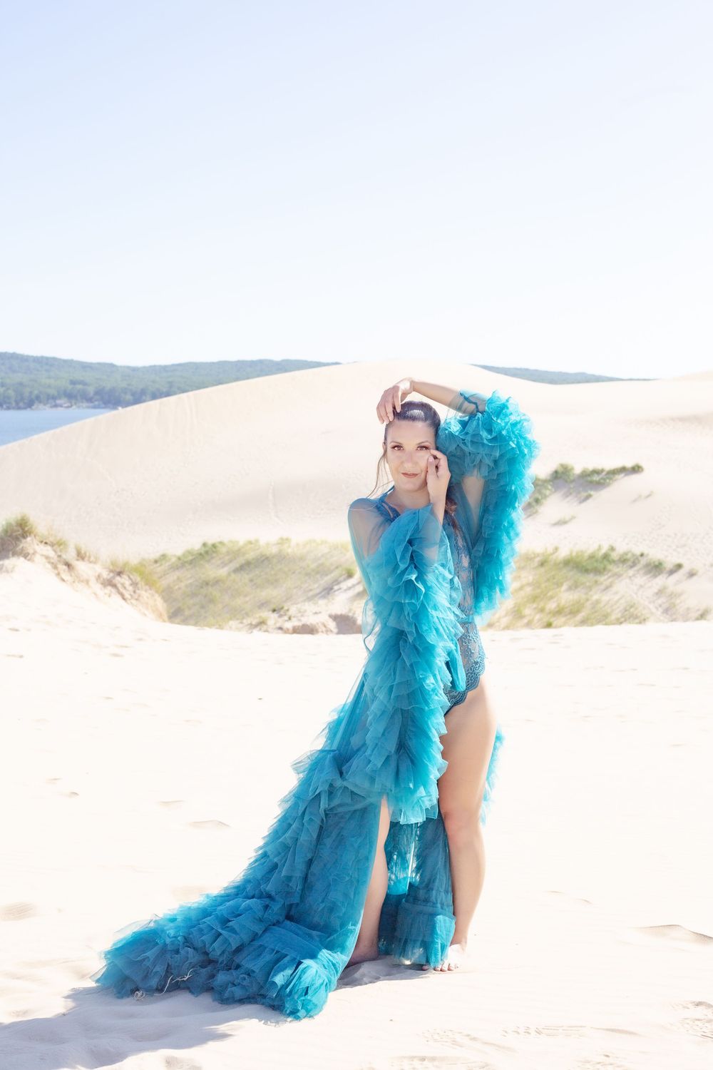 Fashion portrait in turquoise feathered gown on sand dunes under bright sky.