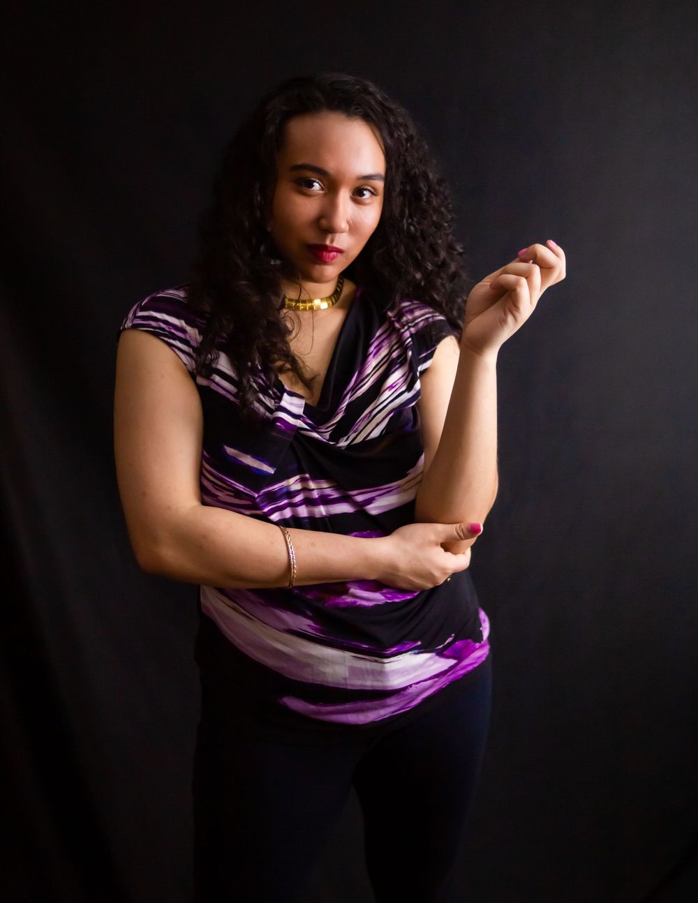 Studio portrait in purple patterned top against black background with dramatic lighting.