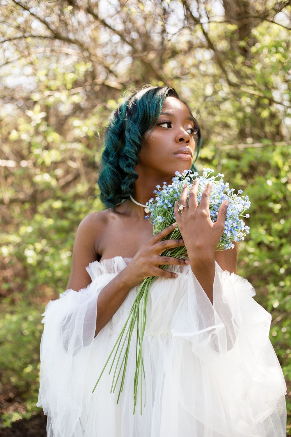 Ethereal portrait of someone wearing a white tulle dress holding delicate white flowers against a soft bokeh background.