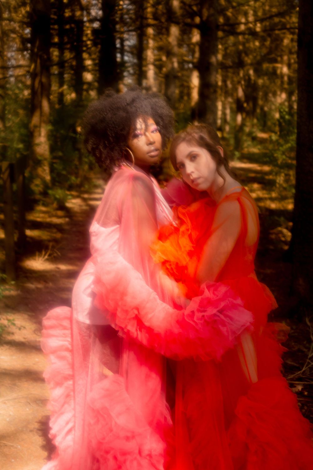 Dreamy forest portrait with two figures in flowing red and coral tulle dresses.