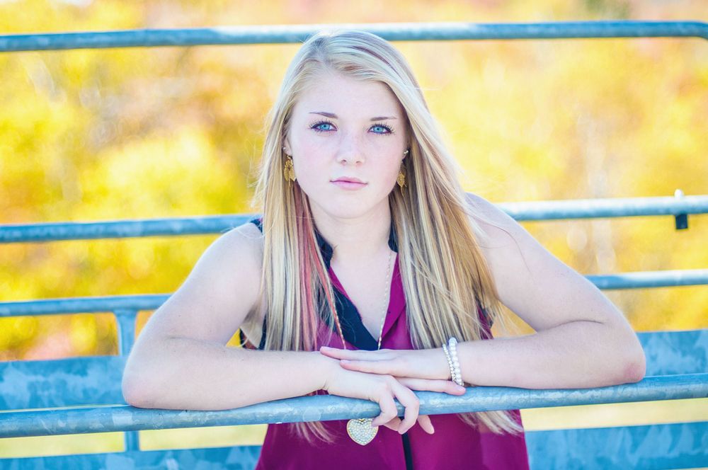 Blonde teenage girl leaning on a yellow railing during an outdoor fall senior portrait session.