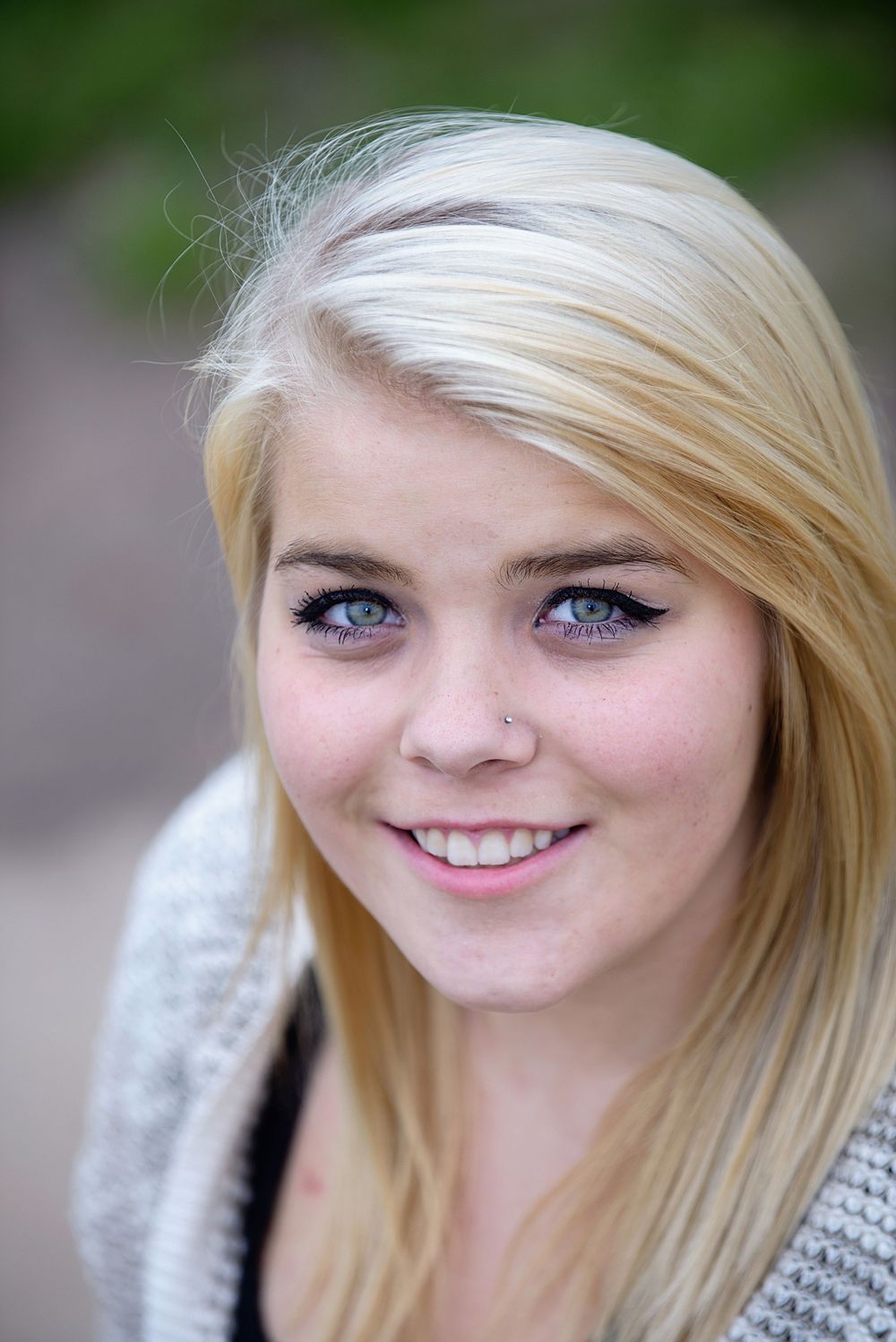 Close-up portrait of smiling blonde teenage girl with blue eyes and nose ring outdoors.