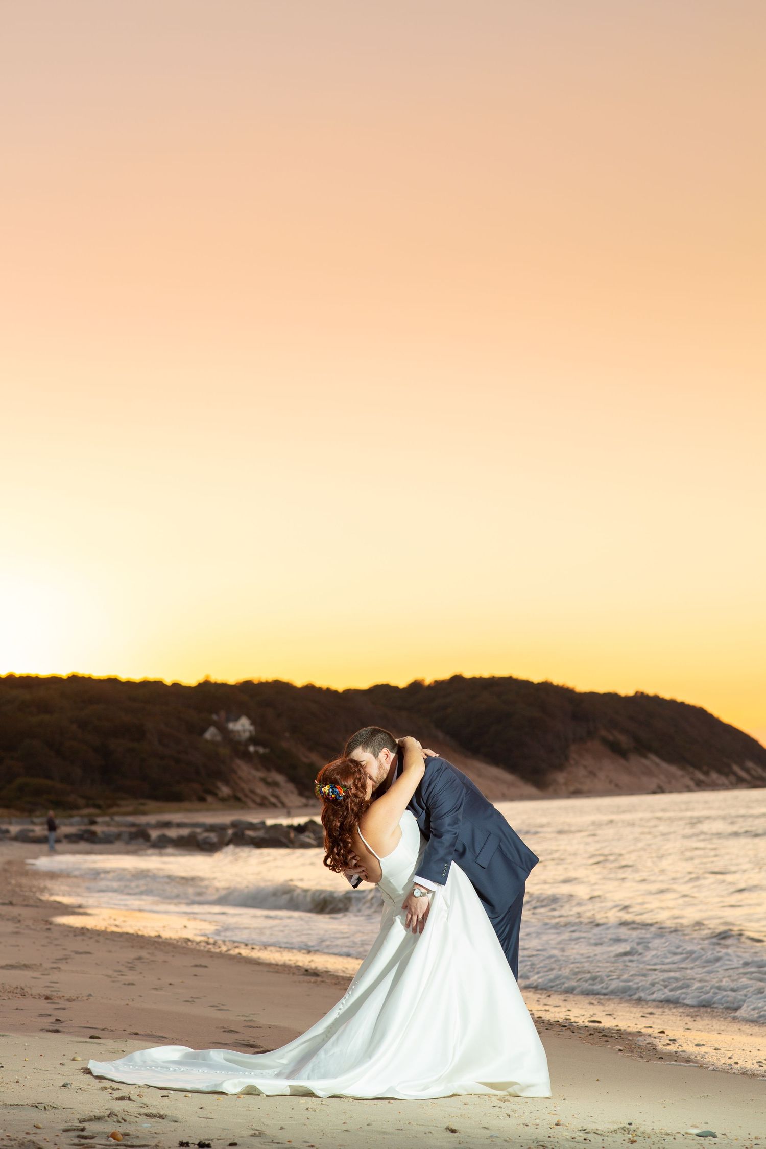 Romantic beach wedding photo during golden hour sunset with couple embracing on sandy shore.