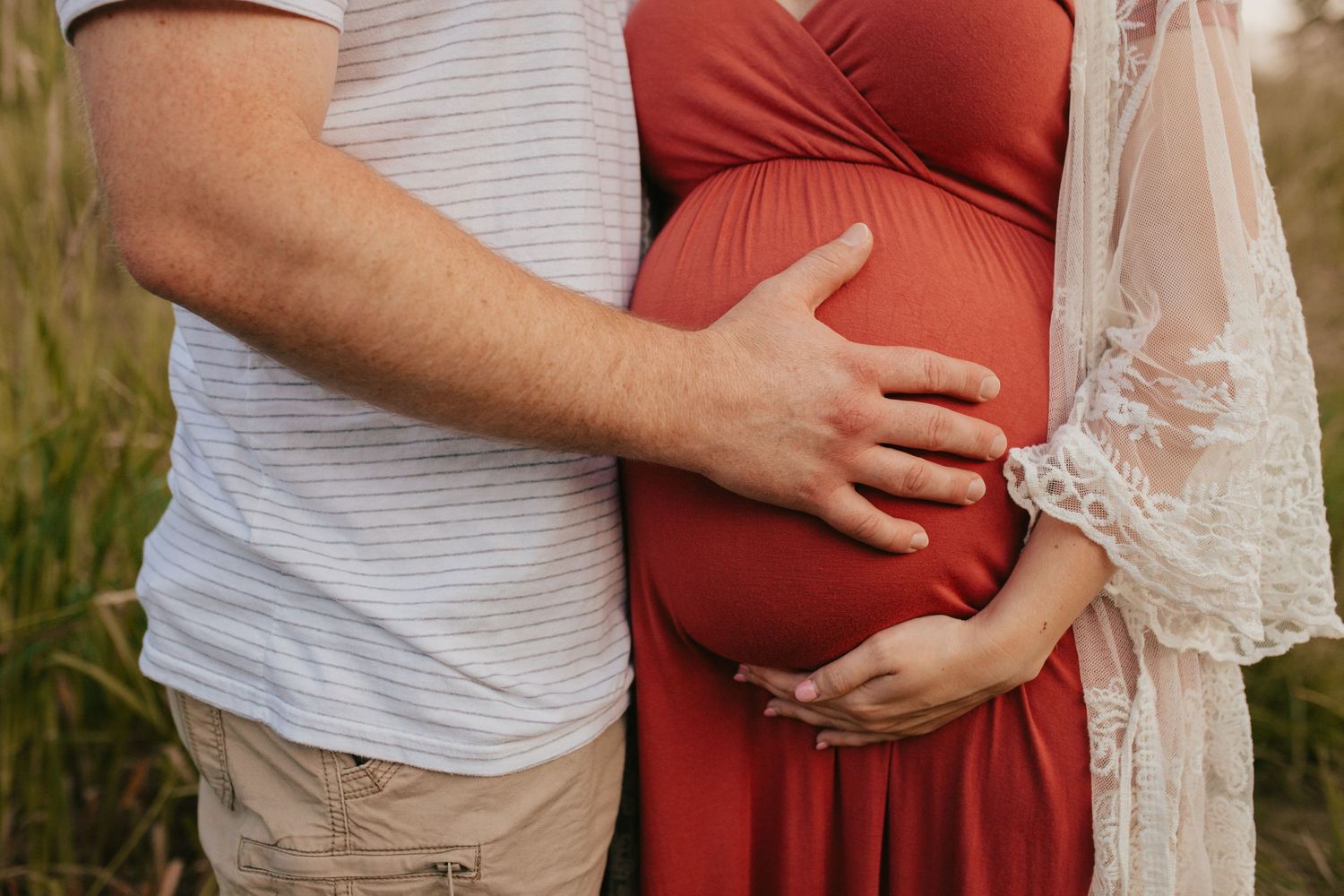 Couple embraces while wearing red and white outfits during a maternity photoshoot.