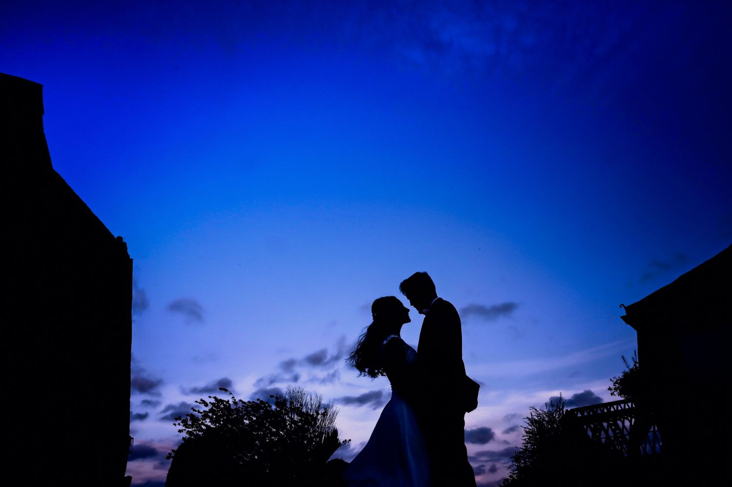 Silhouette of couple against deep blue twilight sky between buildings.