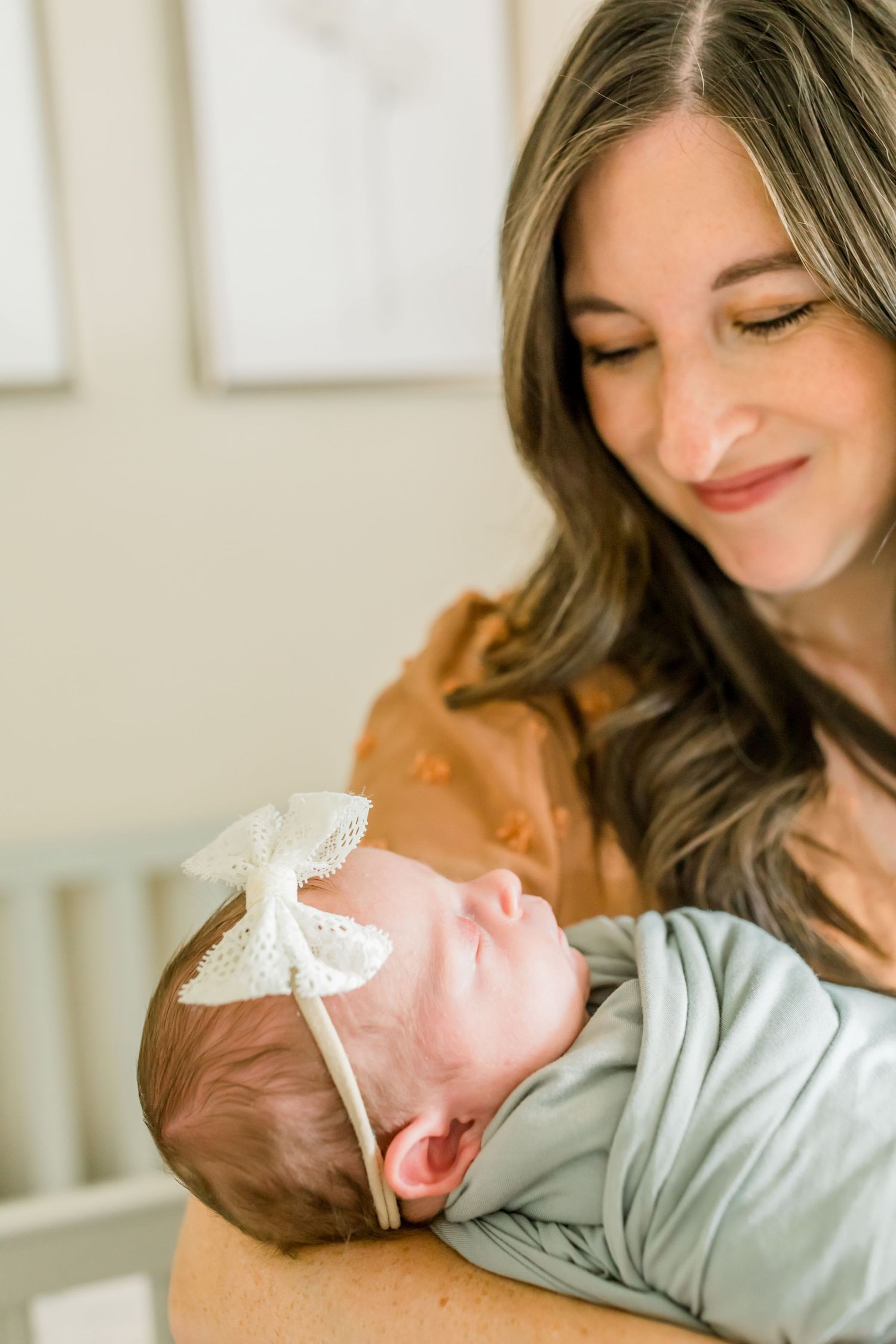 Gentle moment in a nursery featuring a sage swaddled baby and soft window light.