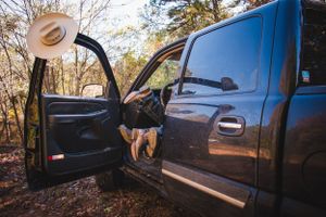 Cowboy hat hangs from open truck door in wooded setting while the Texas couples boots hang out of the door intimately.