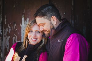 Couple in bright pink and dark clothing sharing a tender moment against rustic backdrop.