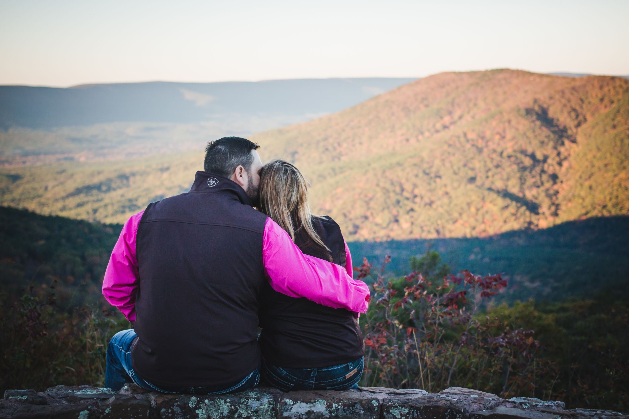 A couple sits together on a rocky overlook enjoying views of autumn mountain vistas in the Oklahoma Arkansas hills along Talimena scenic rd.