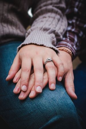 Close-up of clasped hands with an engagement ring resting on denim.