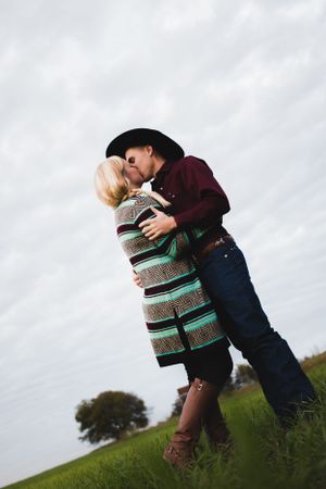 A romantic embrace on a grassy hillside against a cloudy sky.