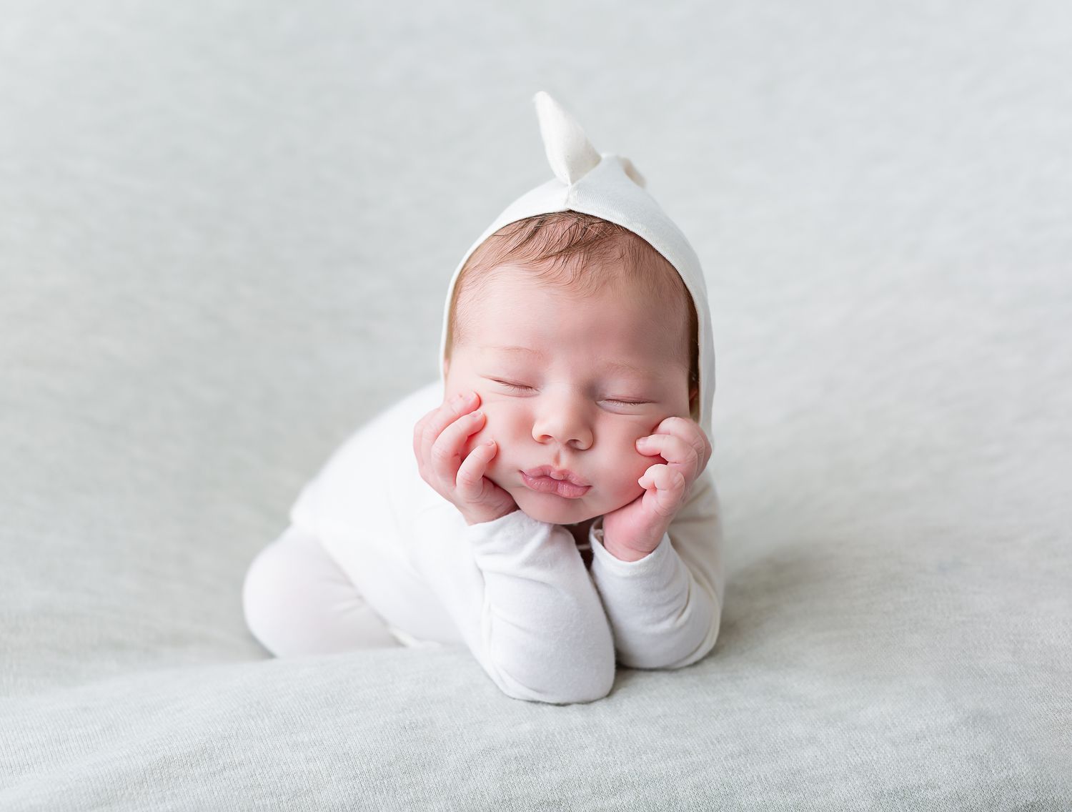Newborn photography series showing peaceful sleeping baby in white against light background.
