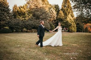 A couple in wedding attire dancing together in a park during golden hour sunset with autumn trees in the background. Rockfield Manor