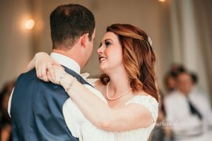 A couple shares their first dance at their wedding reception in an elegant white room with warm lighting. La Banque de Flueve