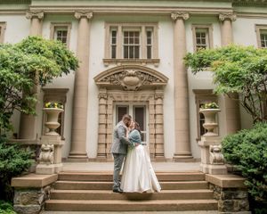 A romantic wedding photo captured on elegant stone steps of a grand mansion with classical columns and architecture.