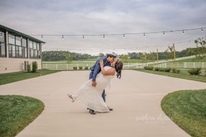 A couple dips and kisses at an outdoor venue with string lights and green grass.