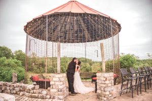 A couple celebrates their wedding under an outdoor gazebo with strung lights and stone pillars during a romantic ceremony.