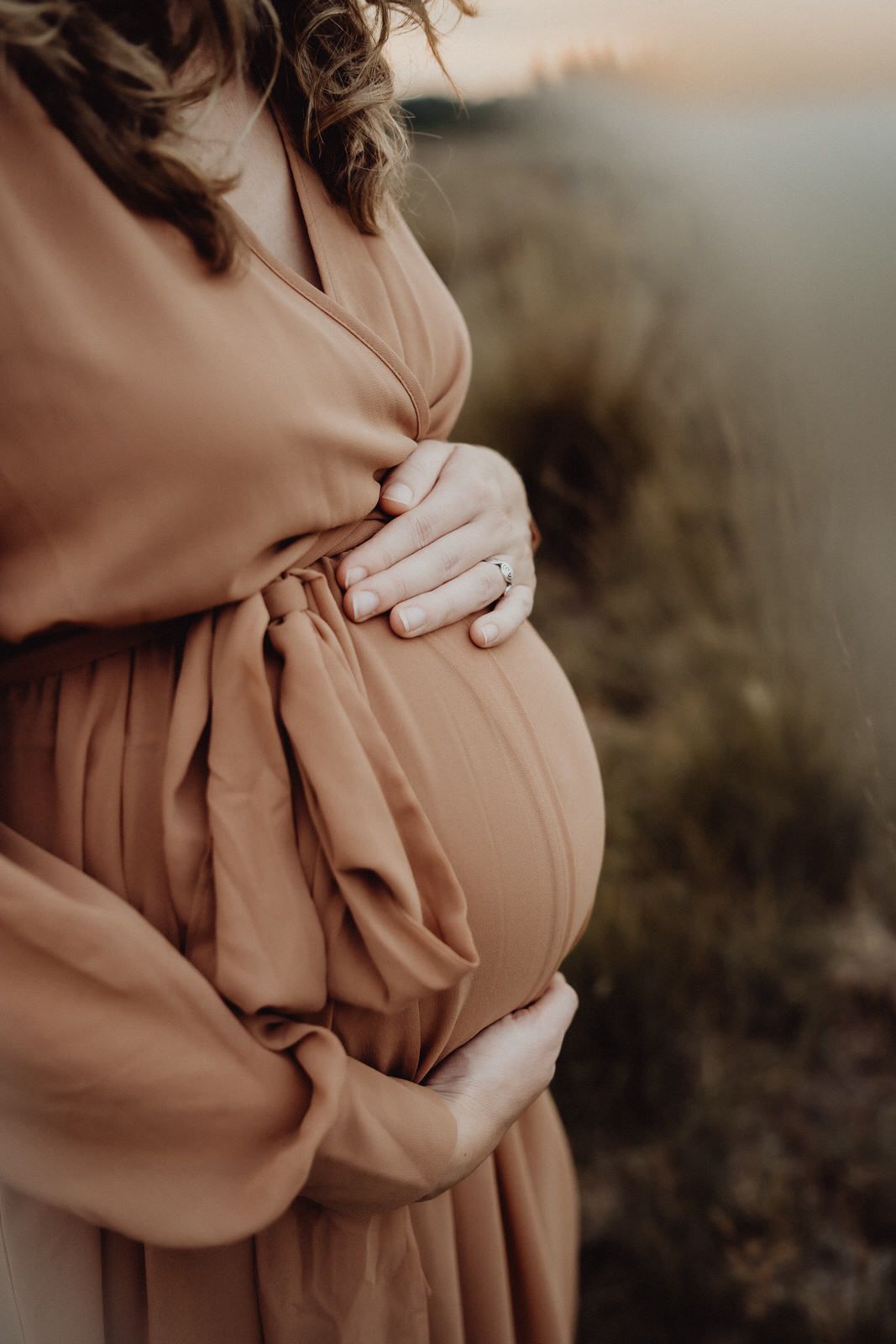 Close-up of hands cradling a pregnant belly in a flowing dusty rose dress.
