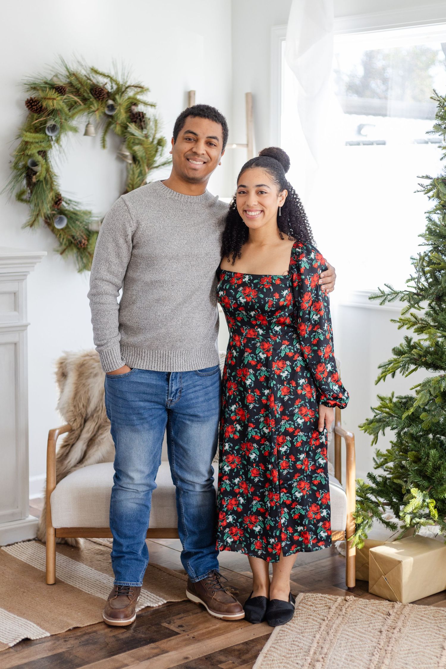 Couple poses in front of Christmas decor wearing casual and floral outfits.