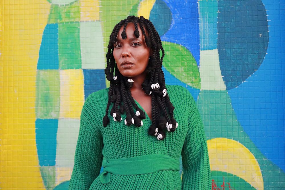 Portrait of someone in a green sweater standing against a colorful geometric mural background.