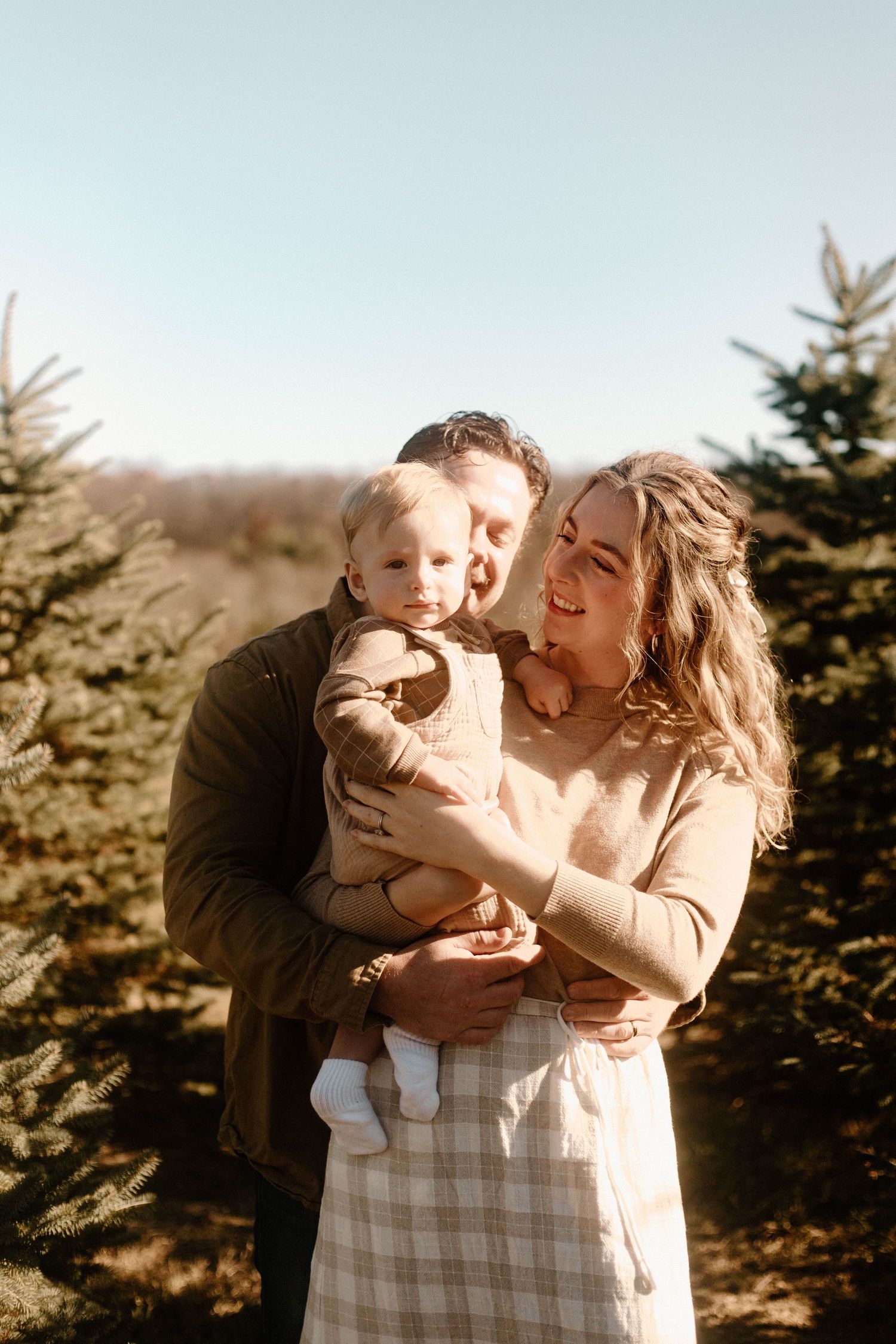 Family shares tender moment together among evergreen trees during outdoor photoshoot.
