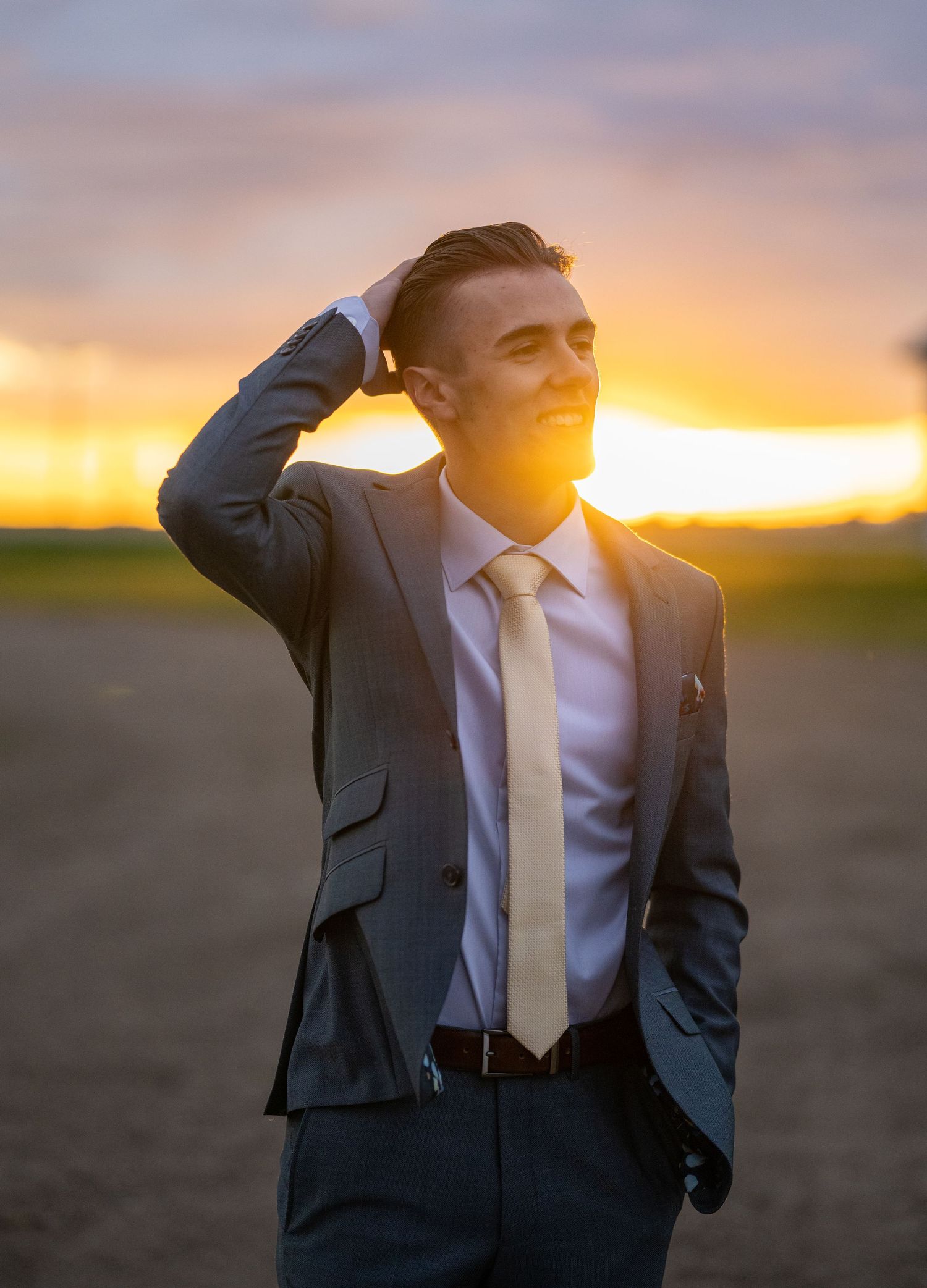 A suited figure stands against a vibrant sunset sky while shielding eyes from the golden light.