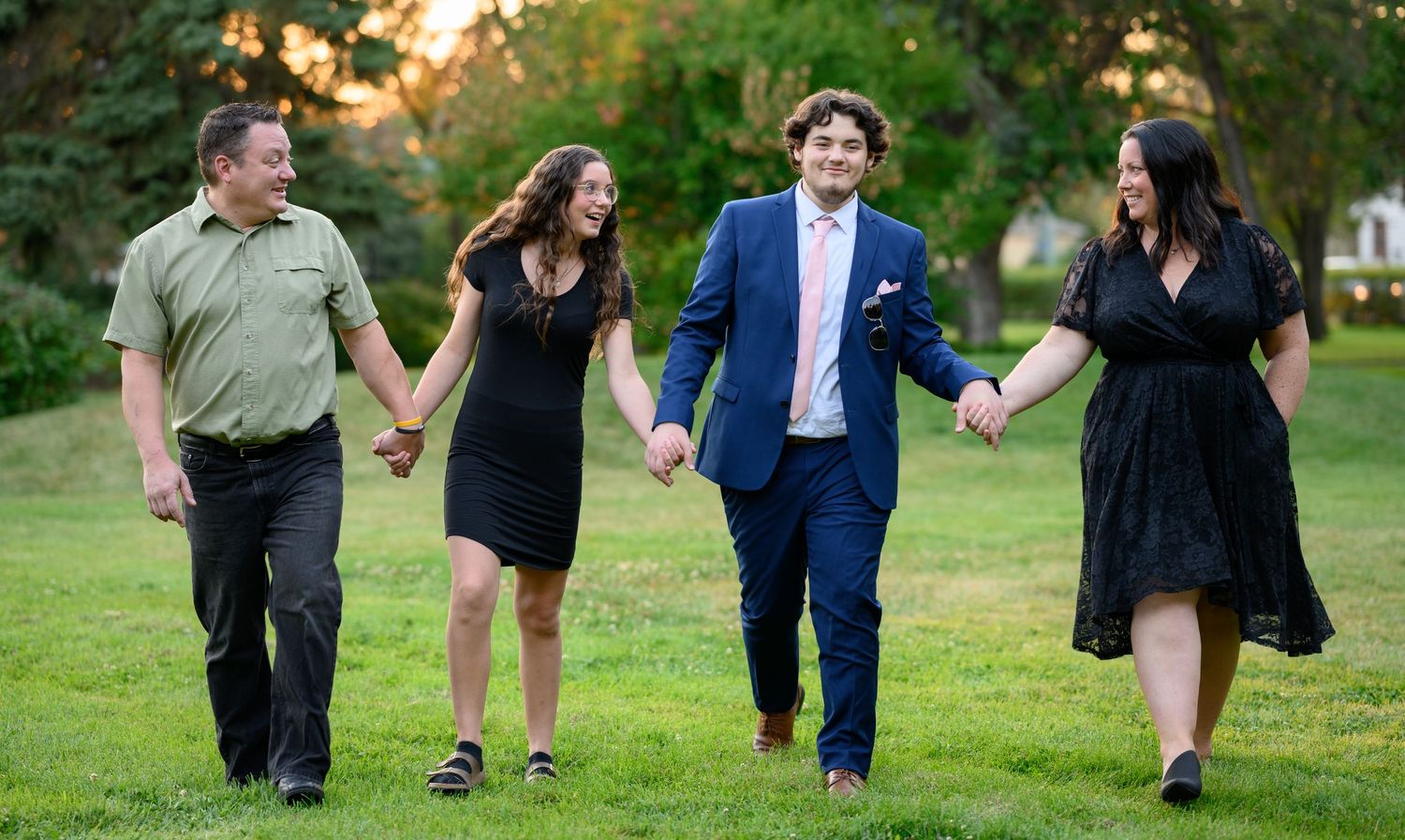 A group of people holding hands while walking together on grass during golden hour.