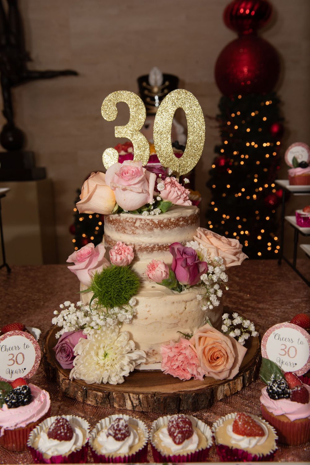 A beautifully decorated 30th birthday cake with fresh flowers and golden topper surrounded by cupcakes.