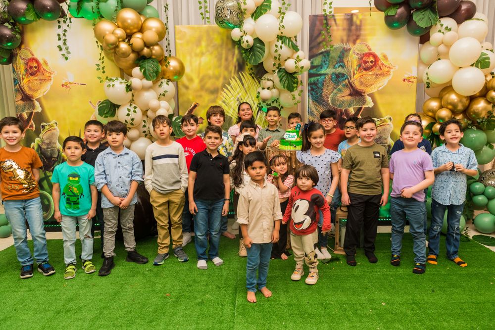 Large group photo of party attendees on artificial grass with balloon decorations.