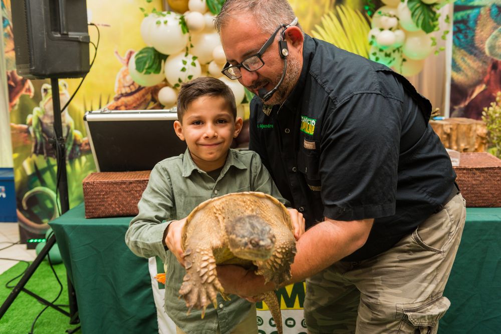 Staff member shows large tortoise to excited child at educational wildlife event.