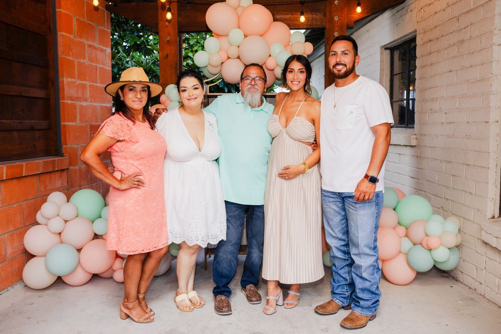 Group photo with pink and mint balloon decorations against brick wall.