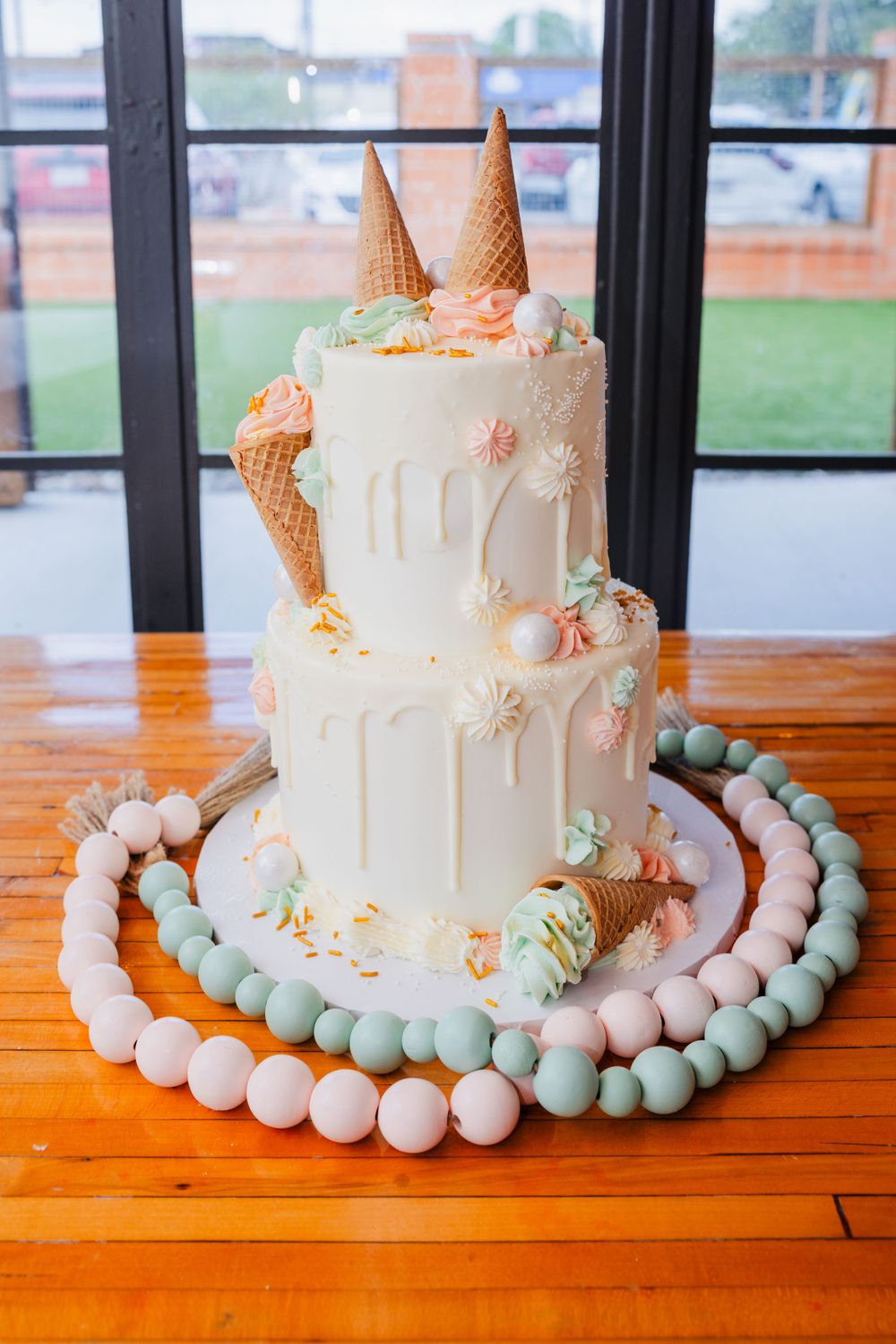 A white drip cake decorated with ice cream cones and pastel macarons arranged in a circle.