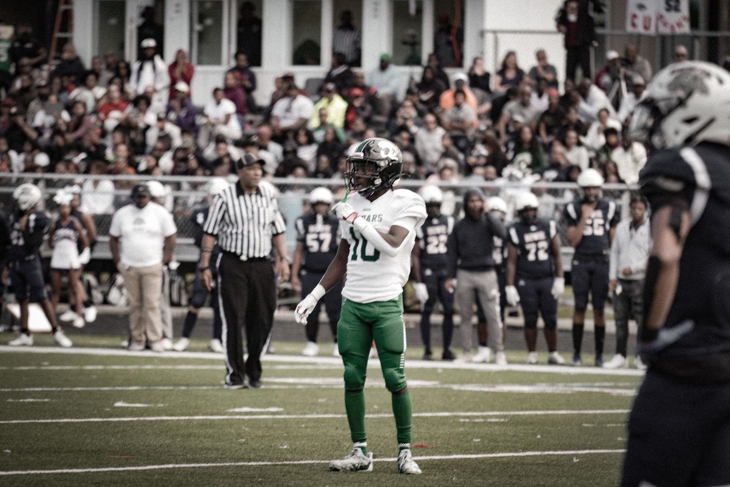 Football player wearing green jersey number 10 stands on field during a college football game with crowd in background.