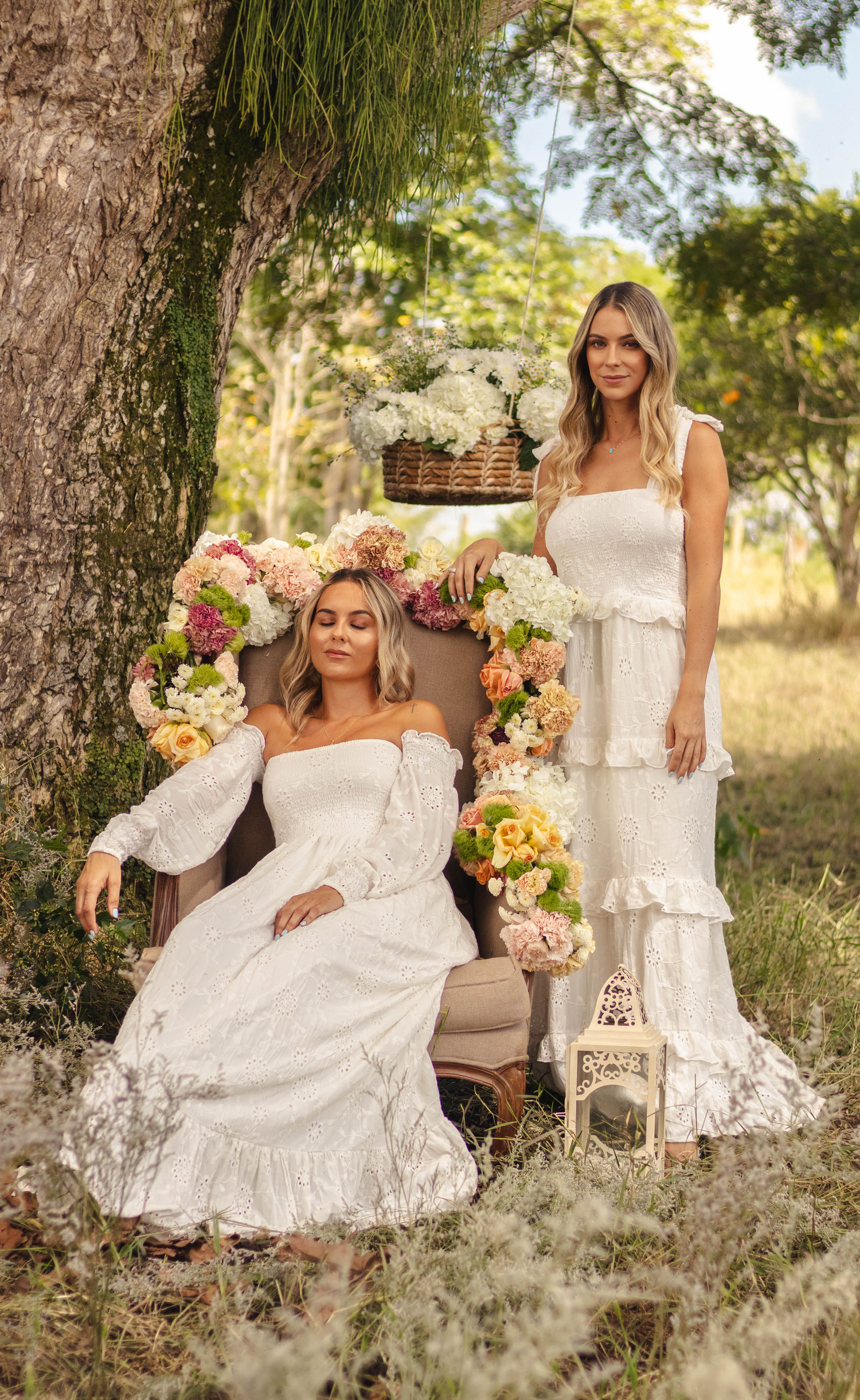 Ethereal garden portrait with women in white dresses posed with floral decorated vintage chair.