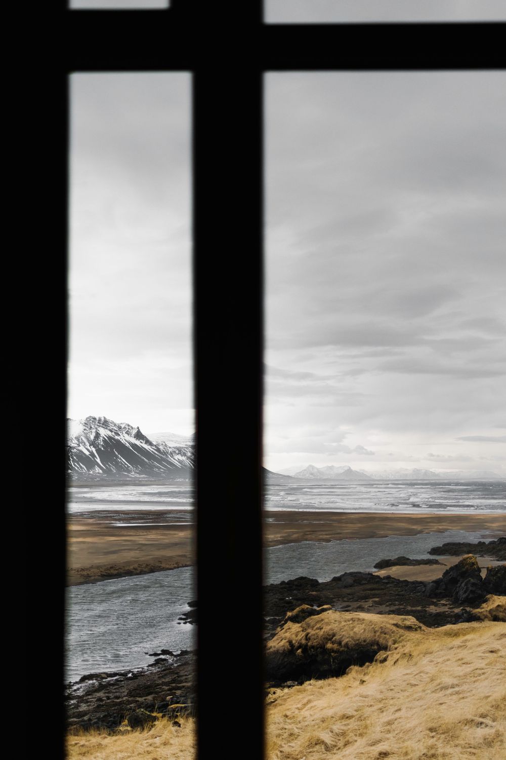 Mountain landscape viewed through window frame showing coastline and rocky terrain.