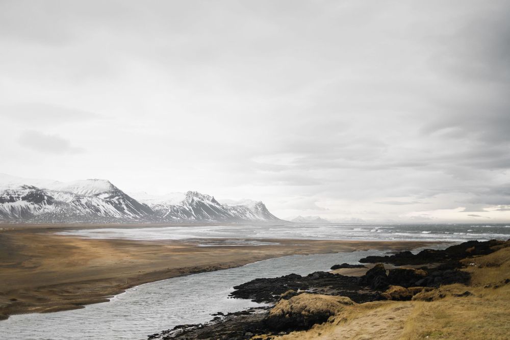 Dramatic landscape of mountains and river in Iceland with overcast skies.