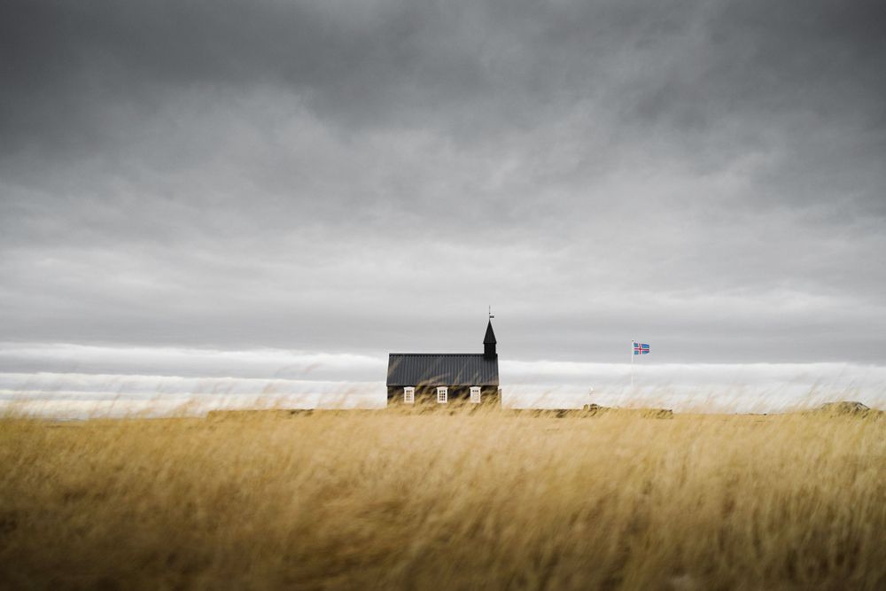 A solitary black house stands in a golden wheat field under moody gray skies.