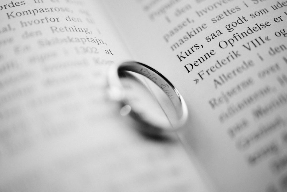 Wedding ring casting shadows on book pages in black and white macro photography.