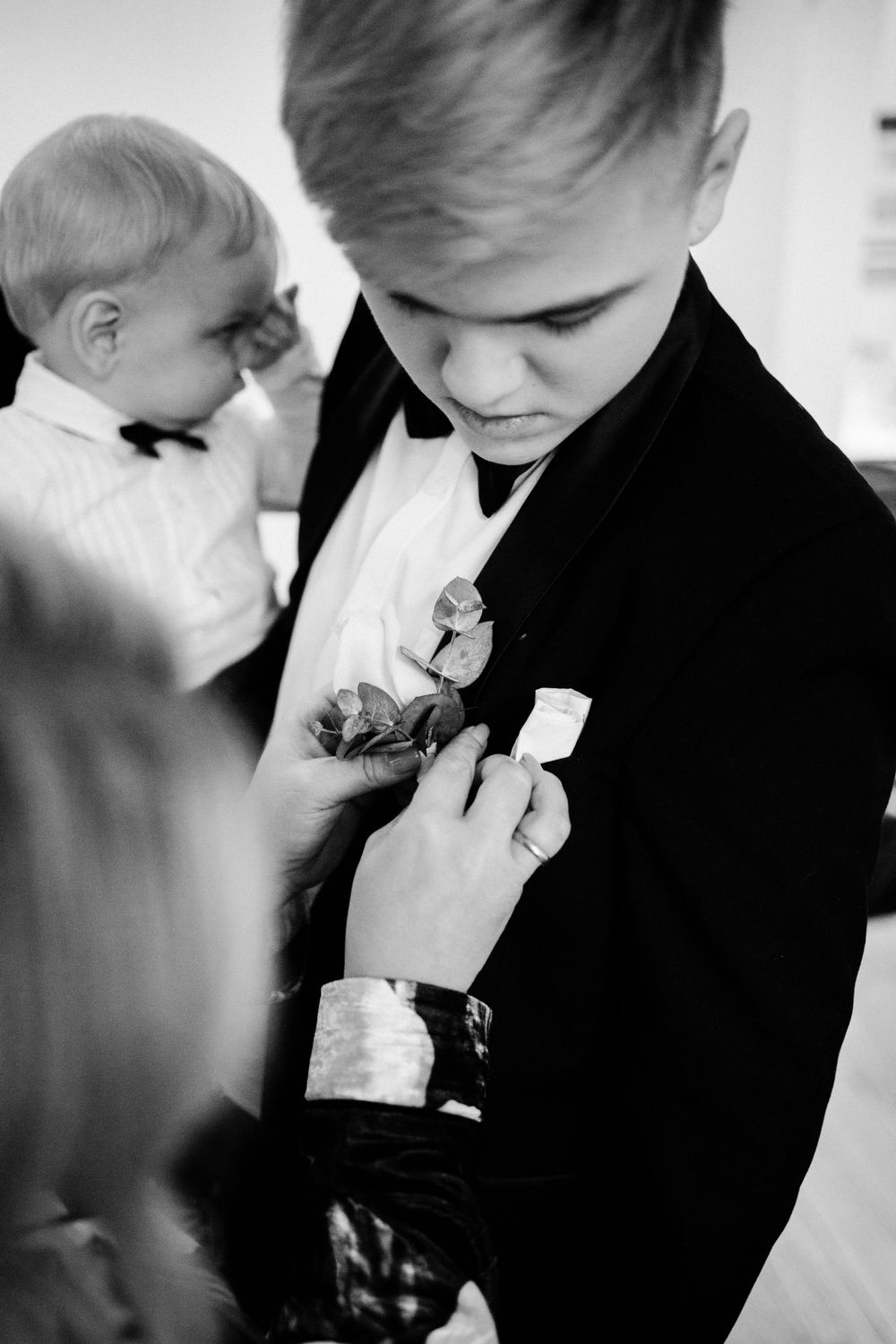 A formal occasion showing the adjustment of a boutonniere on a black tuxedo.
