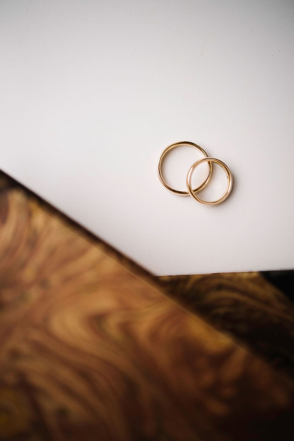 Two gold wedding rings placed on a white surface with wooden texture below.