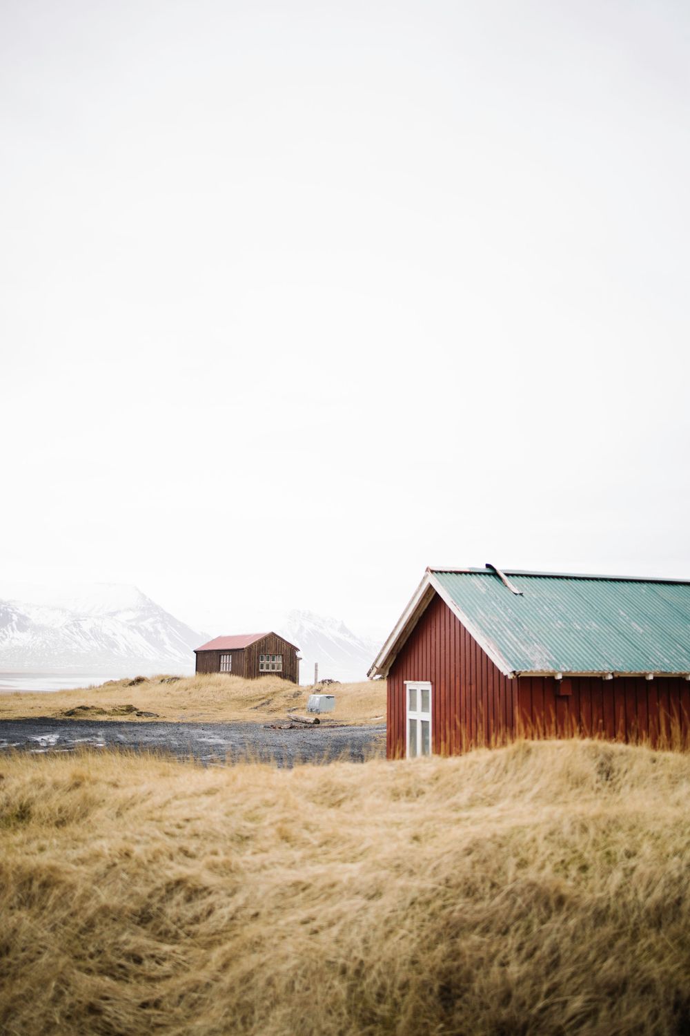 Red and brown cabins stand in a grassy field with snow-capped mountains in the background.