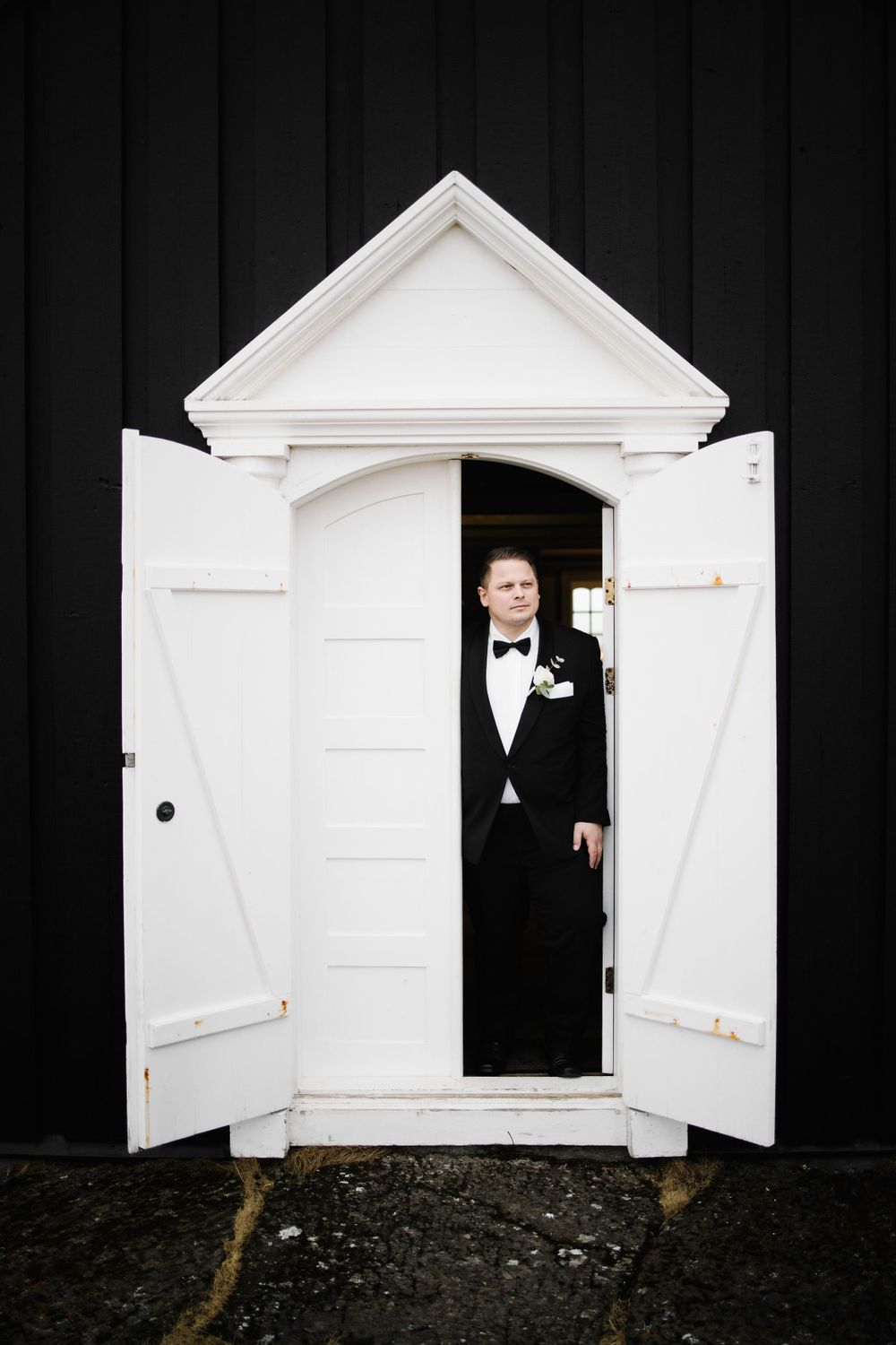 A formal figure stands in a white doorway against a black wall.
